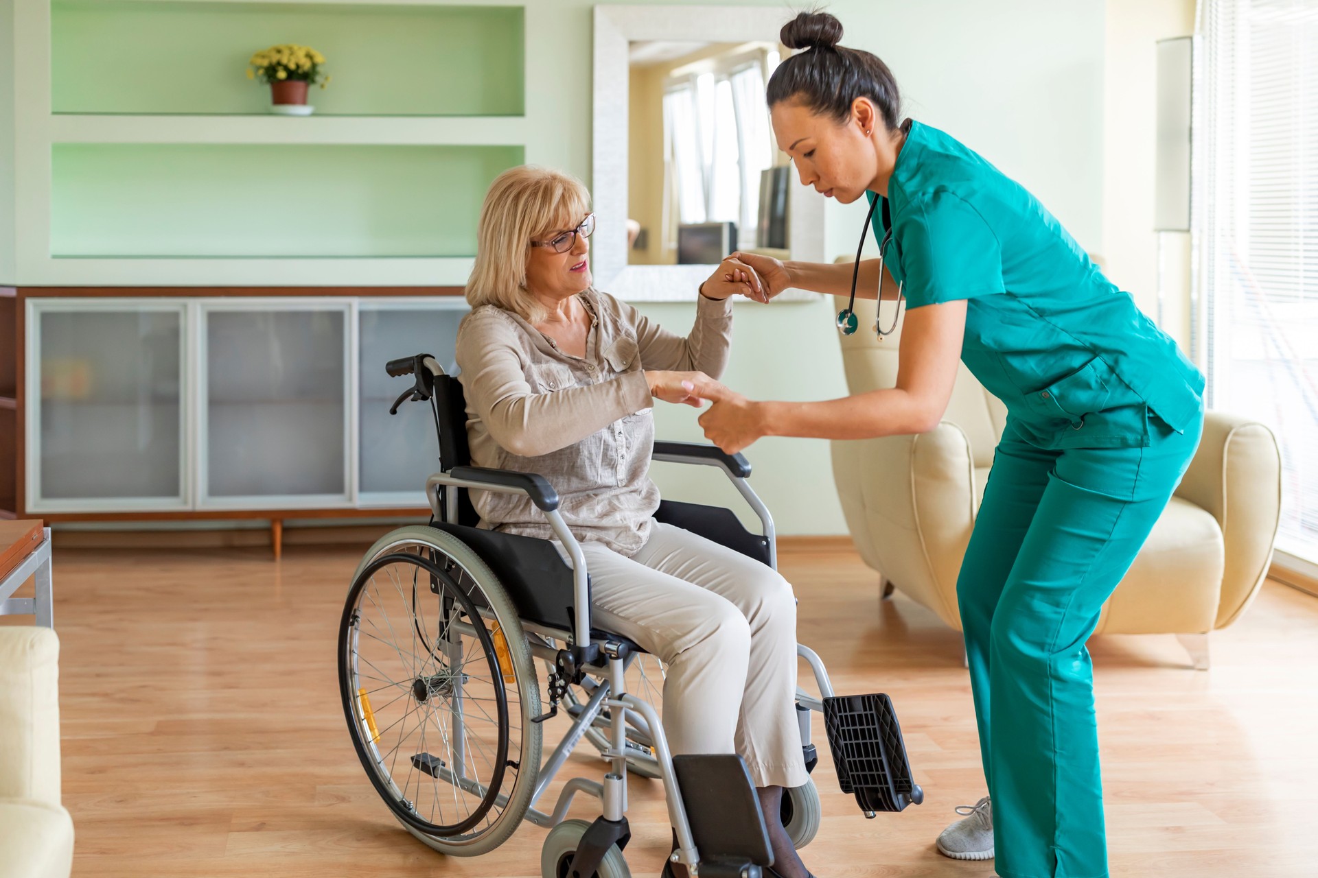 Female Home Caregiver is Helping an Older Woman in Wheelchair to Get up.